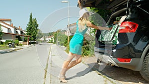 Young blonde woman pushes a suitcase further into the trunk stuffed with luggage