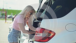 Young blonde woman put her shopping eco bags with food into car trunk on a parking.