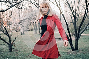 Young blonde woman goes for walk in spring garden on background of blossoming trees.