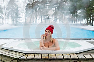 Young blonde woman in red hut in bathtub jacuzzi outdoors at winter