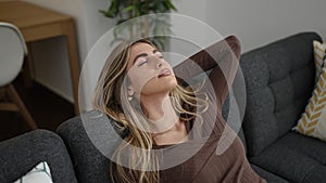 Young blonde woman relaxed with hands on head sleeping on sofa at home