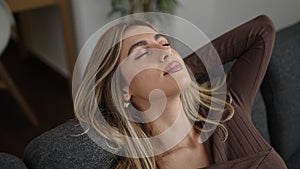 Young blonde woman relaxed with hands on head sleeping on sofa at home