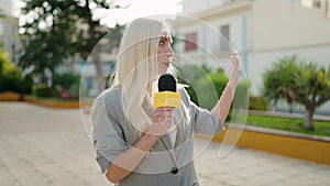 Young blonde woman reporter working using microphone at park