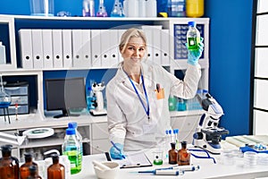 Young blonde woman scientist measuring liquid writing on document at laboratory