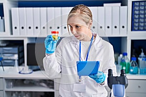 Young blonde woman scientist using touchpad holding urine test tube at laboratory