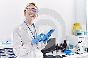 Young blonde woman scientist using touchpad smiling at laboratory