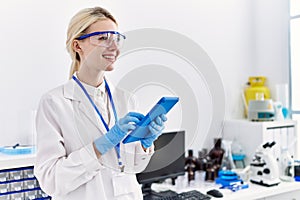 Young blonde woman scientist using touchpad smiling at laboratory