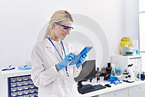 Young blonde woman scientist using touchpad smiling at laboratory