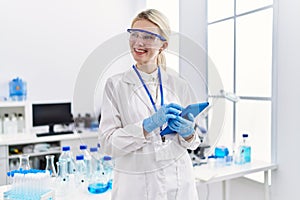 Young blonde woman scientist using touchpad smiling at laboratory