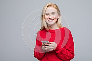 Young blonde Woman sending a sms on cell phone, isolated on gray background