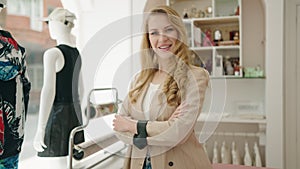 Young blonde woman shop assistant smiling confident standing with arms crossed gesture at clothing store