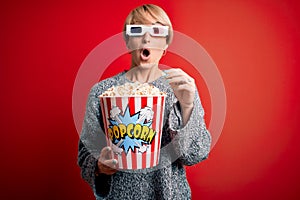 Young blonde woman with short hair wearing 3d movie glasses and eating popcorn at the cinema scared in shock with a surprise face,