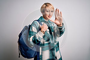 Young blonde woman with short hair wearing travel backpack over  background with open hand doing stop sign with serious