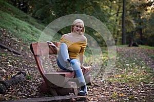 Young blonde woman sitting alone on a wooden bench in the forest