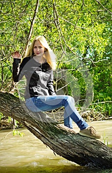 Young blonde woman sitting on dried-up tree