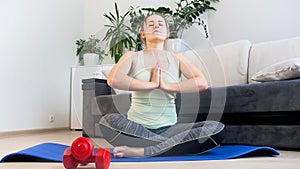 Young blonde woman sitting in lotus yoga positin at home