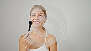 Young blonde woman smiling confident holding makeup brush over isolated white background