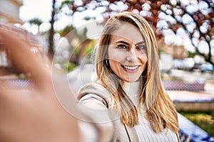 Young blonde woman smiling confident make selfie by the smartphone at street