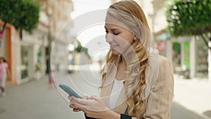 Young blonde woman smiling confident making photo by the smartphone at street