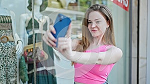 Young blonde woman smiling confident making selfie by the smartphone at clothing store