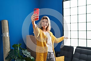 Young blonde woman smiling confident making selfie by the smartphone at new home