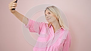 Young blonde woman smiling confident making selfie by the smartphone over isolated pink background