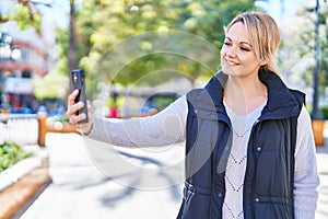 Young blonde woman smiling confident making selfie by the smartphone at park