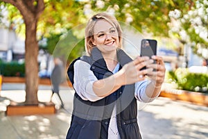 Young blonde woman smiling confident making selfie by the smartphone at park