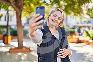 Young blonde woman smiling confident making selfie by the smartphone at park