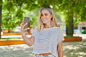 Young blonde woman smiling confident making selfie by the smartphone at park