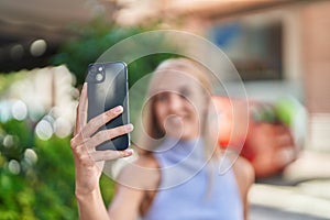 Young blonde woman smiling confident making selfie by the smartphone at street