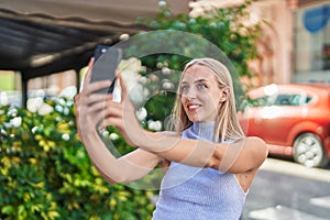 Young blonde woman smiling confident making selfie by the smartphone at street