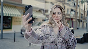 Young blonde woman smiling confident making selfie by the smartphone at street