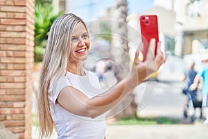 Young blonde woman smiling confident making selfie by the smartphone at street