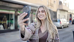 Young blonde woman smiling confident making selfie by the smartphone at street