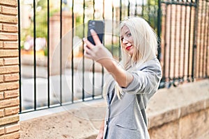 Young blonde woman smiling confident making selfie by the smartphone at street