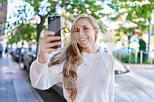 Young blonde woman smiling confident making selfie by the smartphone at street