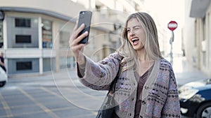 Young blonde woman smiling confident making selfie by the smartphone at street