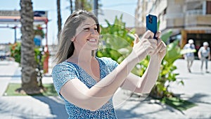 Young blonde woman smiling confident making selfie by the smartphone at street