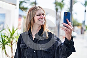 Young blonde woman smiling confident making selfie by the smartphone at street