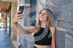 Young blonde woman smiling confident making selfie by the smartphone at street