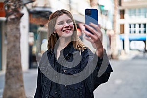 Young blonde woman smiling confident making selfie by the smartphone at street