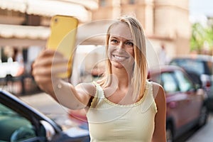 Young blonde woman smiling confident making selfie by the smartphone at street