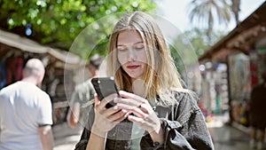 Young blonde woman smiling confident making selfie by the smartphone at street market