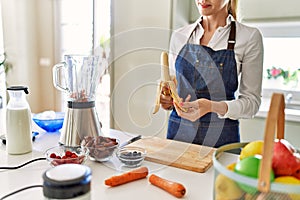 Young blonde woman smiling confident peeling banana at kitchen