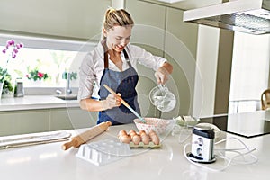 Young blonde woman smiling confident pouring water on bowl at kitchen