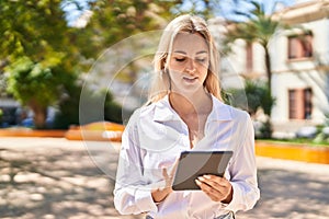 Young blonde woman smiling confident using touchpad at park