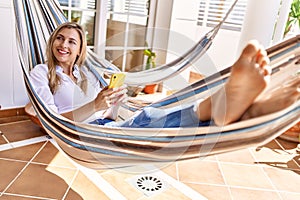 Young blonde woman smiling happy lying on hammock at terrace