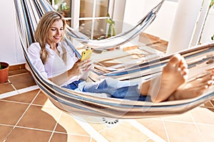 Young blonde woman smiling happy lying on hammock at terrace