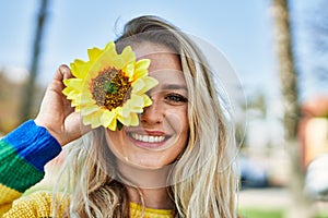 Young blonde woman smiling with sunflower on eye at the park